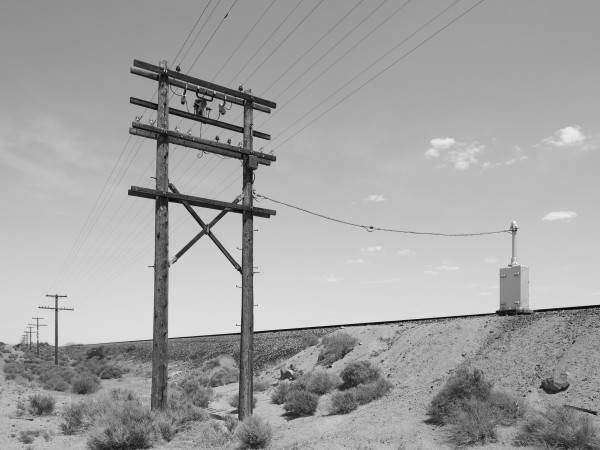 Wooden pylons supporting telegraph wires, going off into the distance alongside railroad tracks.