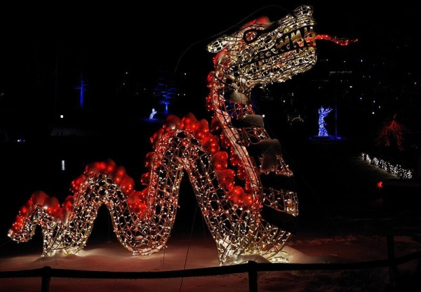 A night image of a dragon made of light in red and white with its thoung haniging out. In the background a unicorn, an angel and some lit up trees are visible.