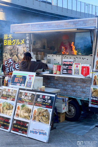 A food truck vendor in Tokyo is using a fairly big open fire inside their food truck to prepare their lunch offerings for office workers.