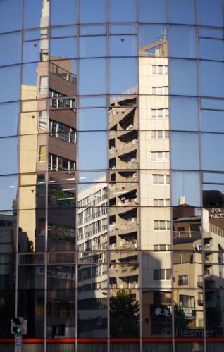 Hohe Häuser einer Grosstadt spiegeln sich in der gebogenen Glasfasade eines Hause