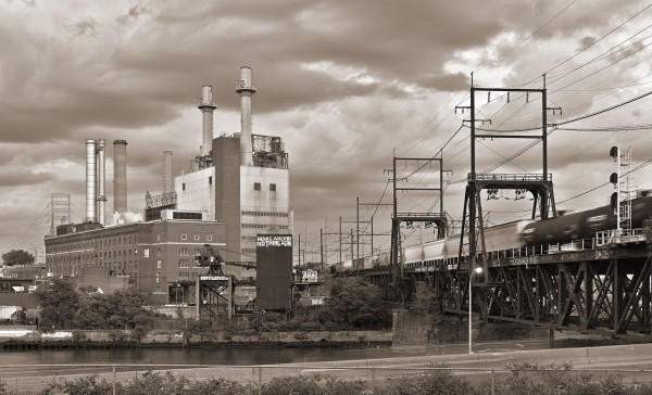 A power plant, with five prominent smokestacks, and a railroad draw bridge carrying a freight train.