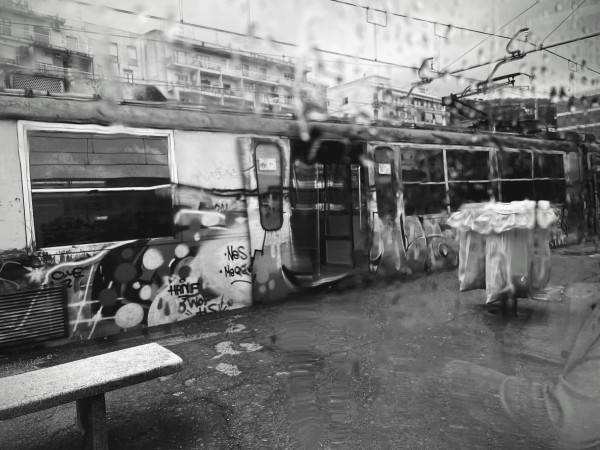 This is a black and white photograph of a graffitied train that was taken from inside an adjacent train at the station. The image is obscured by the rain collected from the outside of the window.